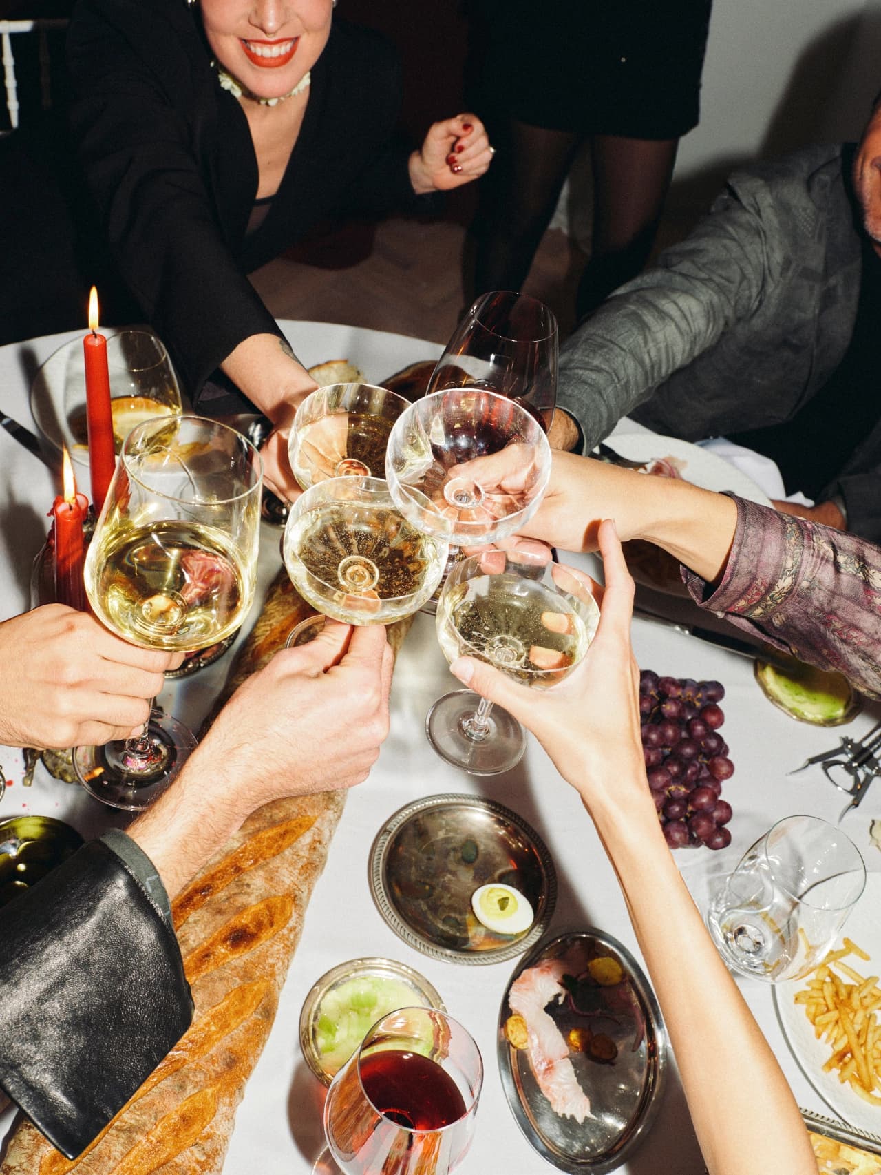 Hands reaching across a dinner table to toast with champagne and wine